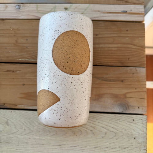 Cylindrical ceramic object with brown accents on a wooden surface